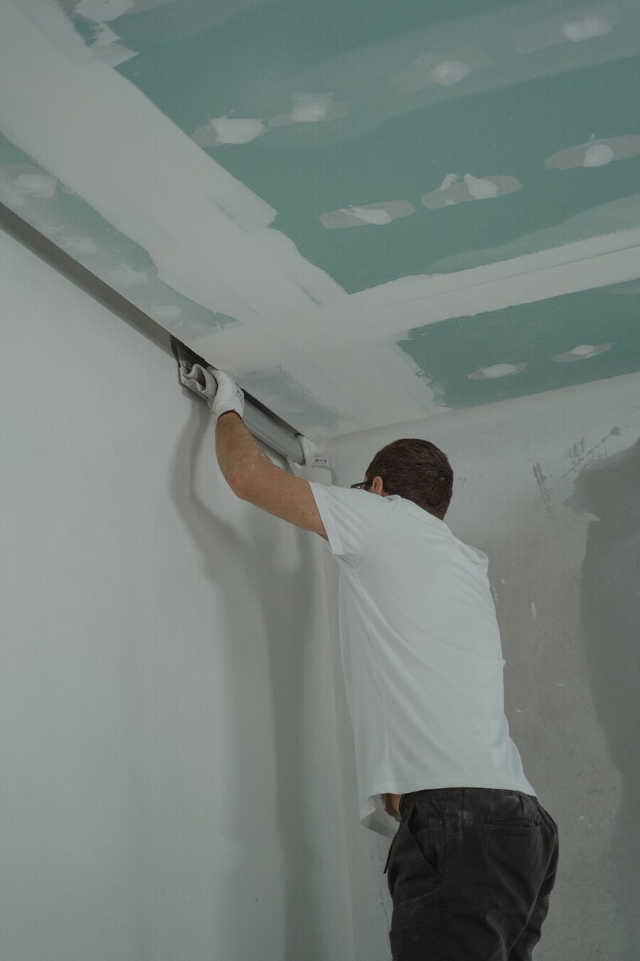 Handwerker arbeitet auf einer Leiter an einer Gipsdecke in einem Rohbau
